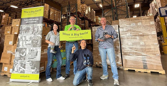 A Wear A Big Smile Foundation banner display stands next to a van loaded with Washington Shoe Company boxes in a parking lot.