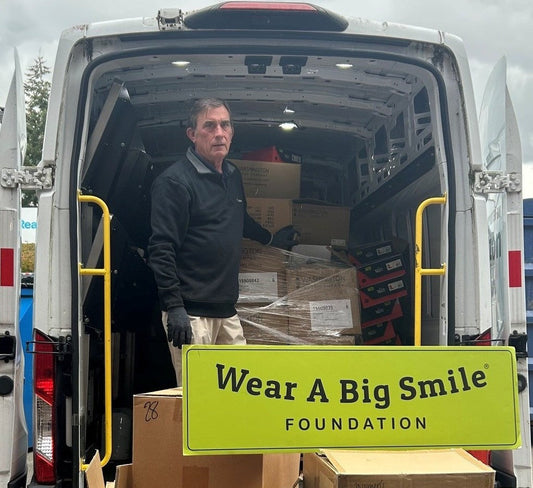 A Wear A Big Smile volunteer standing in the back of an open delivery van loaded with boxes of donated Washington Shoe Company boots and shoes.